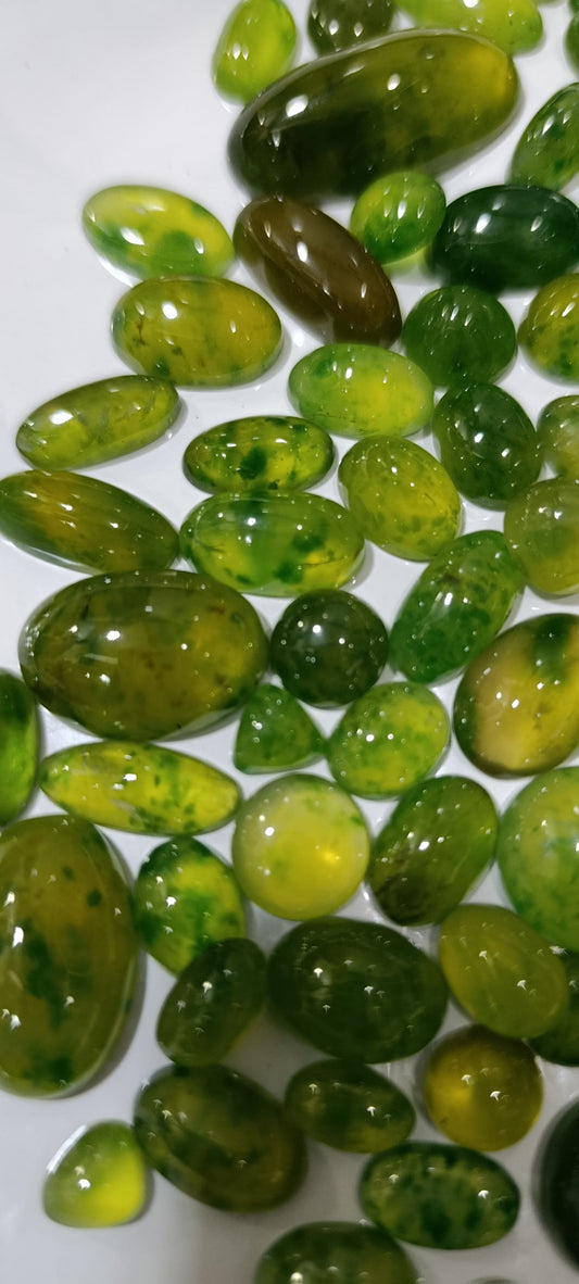 A pile of polished green gemstone beads with natural marbling and inclusions, displayed on a white background.