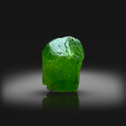 Green peridot crystal on a reflective black surface with a dark background