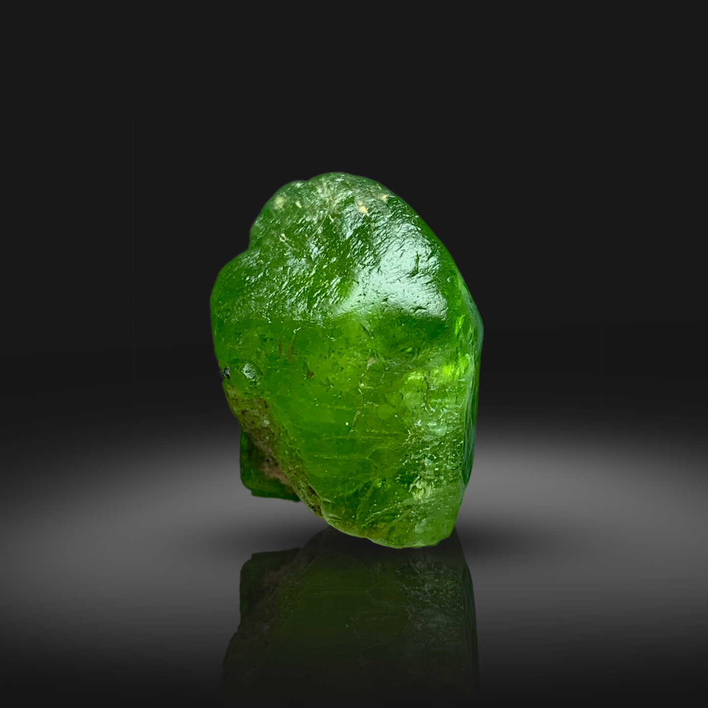 Green peridot crystal on a reflective black surface with a dark background