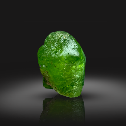 Green peridot crystal on a reflective black surface with a dark background