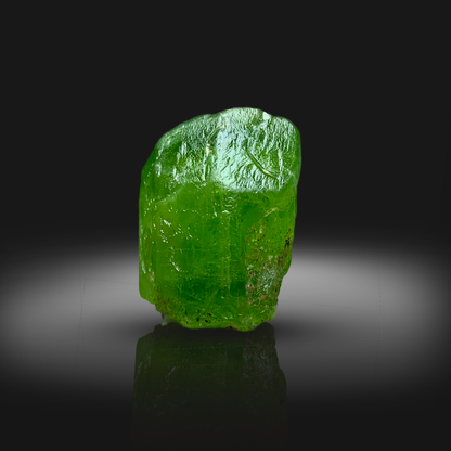 Raw green peridot on a reflective black surface with a dark background