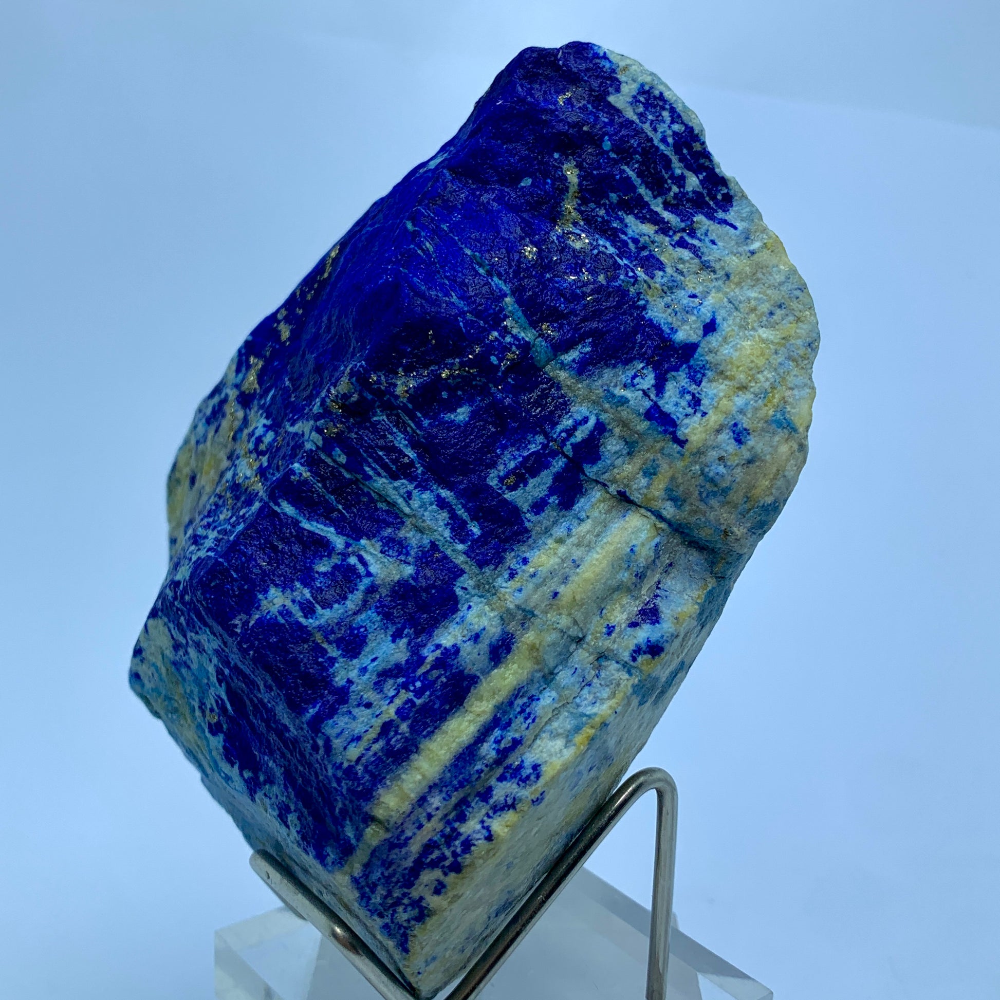 Blue mineral specimen on a stand against a light blue background