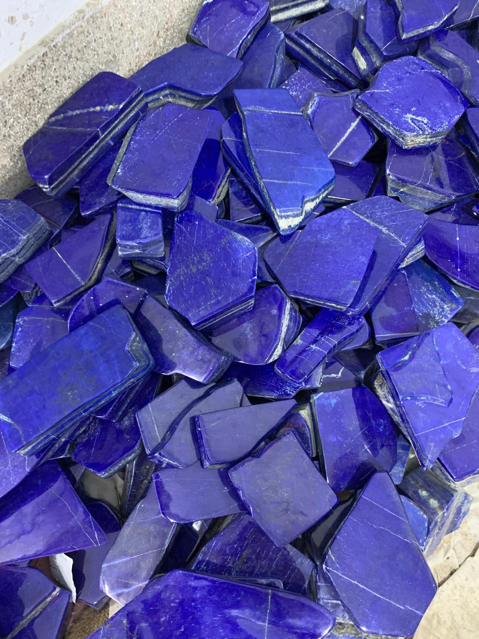 A pile of polished raw lapis lazuli crystal chips in deep blue-violet colors with natural white veining, filling the frame.