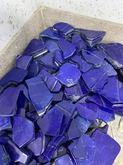 A pile of polished blue lapis lazuli crystal chips with visible white veining, resting inside a light-colored concrete container.