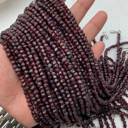 Multiple strands of faceted dark red gemstone beads draped over a person's hand, with some loose strands and silver clasp ends visible on a light surface.