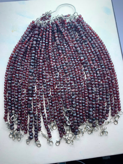 A handmade beaded fringe accessory featuring multiple strands of small round beads in maroon, burgundy, and gray, finished with silver metal lobster clasps at the bottom, displayed on a light surface.